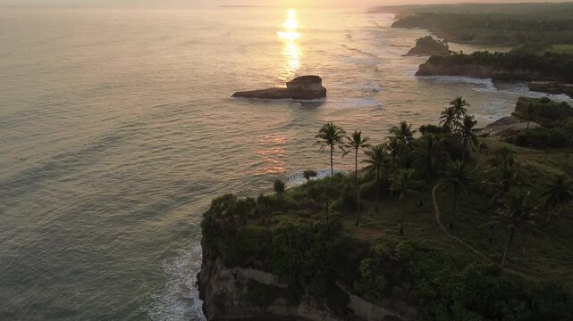 Aerial shot of sunset view with palm trees at Karang Gantungan beach, Sukabumi, Indonesia.