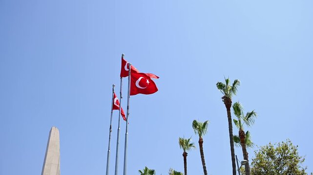 Turkish national flags waving on flagpoles against blue sky in sunny park. Turkey republic pride, Mediterranean travel and patriotism , concept. Red flags with white crescent and star