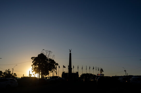 Silhouette of the Obelisco de Las Piedras during sunset in Parque Artigas, Las Piedras, Uruguay. Urban travel landmark with flags, dramatic sky and copy space.