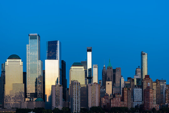 Modern architectural glass facades of office towers in the Financial District reflect the remaining light of dusk over the Hudson River.