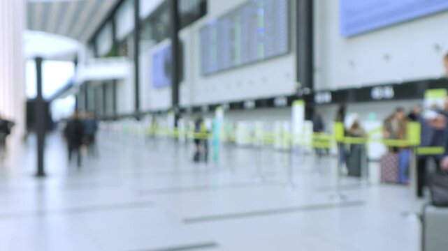 Blurred airport terminal with travelers walking. People carry luggage near check-in counters. Digital screens and yellow barriers visible. Indoor lighting reflects on polished floor