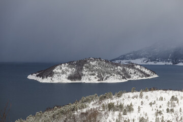 Snow-covered island in Malangen fjord near Tromso, Norway. Calm dark water contrasts with white winter landscape, creating peaceful Arctic scene with remote Nordic wilderness © Fauren