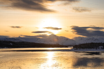 Obraz premium Golden sunset over frozen Malangen fjord in northern Norway with snow-covered mountains in silhouette. Warm Arctic light reflects on calm water. Crazy Hallo effect