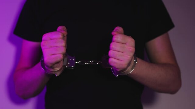 Steel handcuffs. Man in a black T-shirt. Slow motion video. High quality 4k footage