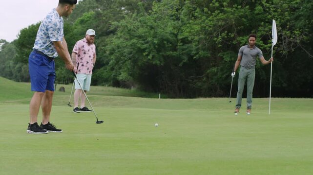 A man putts his ball into the hole and misses as two of his friends watch.