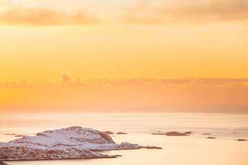 Naklejka premium Golden sunset over a fjord on Kvaloya, Norway, with sun rays spreading above snow-covered mountains