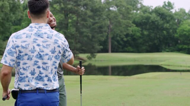 Two male friends fist bump each other as one of them puts a golf ball on a tee to prepare his shot