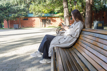 Fototapeta premium Pretty woman using smartphone and sitting on bench outdoors