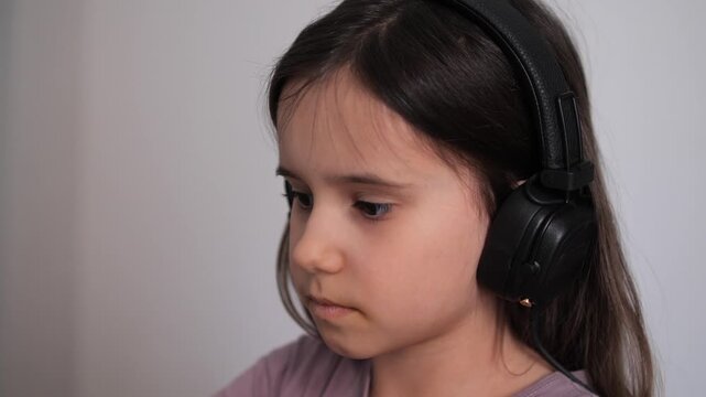 Young girl with long dark hair wearing black over ear headphones, intently listening to digital lessons or entertainment while studying or learning at home, focused and absorbed