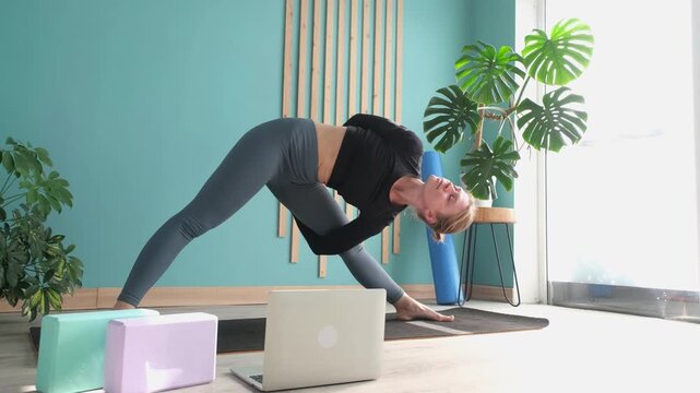Young attractive woman practicing yoga standing in extended triangle pose or trikonasana pose in yoga studio or at home