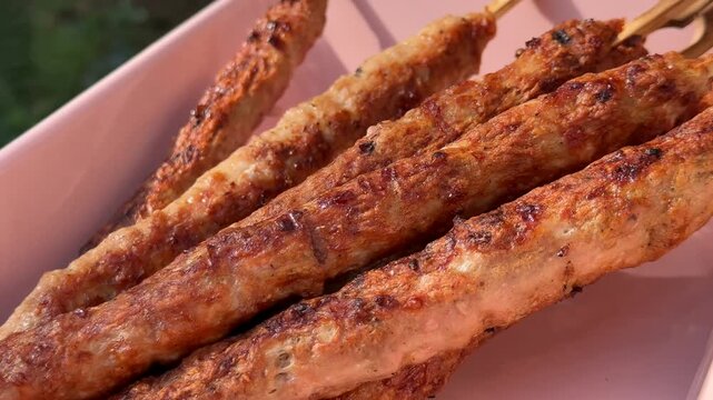 Grilled meat kebabs on a white plate, browned and lightly charred, served outdoors in warm light, conveying a casual barbecue meal and appetizing comfort