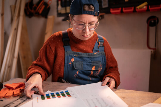 Female carpenter business owner analyzing profit charts and documents in workshop