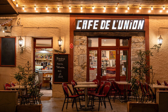 Cotignac, Provence-Alpes-C&ocirc;te d&rsquo;Azur, France, 3 April 2026: facade of Cafe de l&rsquo;Union with outdoor terrace and illuminated sign at night in a traditional Proven&ccedil;al village