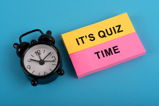 Alarm clock and colored paper note with text It's Quiz Time