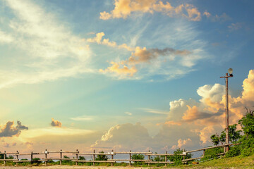 Naklejka premium Golden sunset sky with clouds and rustic fence in a peaceful countryside creating a warm natural landscape background with copy space