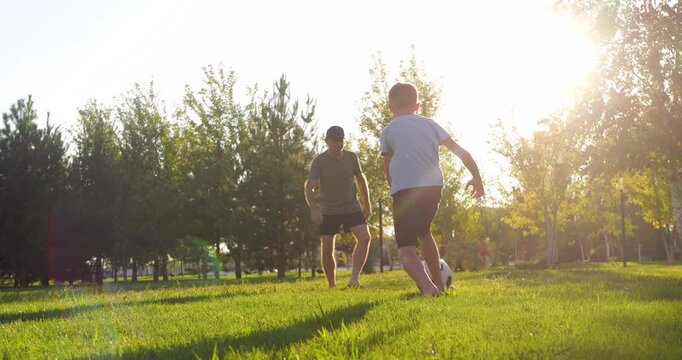 Happy father and son playing soccer in park at sunset. Joiful dad and kid. Active outdoor family time, childhood fun and healthy lifestyle. Family bonding moments create lasting memories.