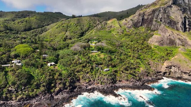Aerial Drone footage of Pitcairn Islands Over Clear Blue Ocean. Volcanic coast ocean showcasing rugged green slopes, basalt cliffs, scattered village houses, crashing white waves over coral