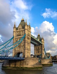 Obraz premium A tall, stone bridge against a bright blue sky filled with fluffy white clouds, casting a slight shadow on the bridge