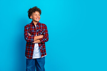 Fototapeta premium Smiling confident boy in red plaid shirt standing with arms crossed against bright blue background, casual youth portrait conveying happiness and optimism