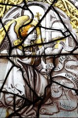 Fototapeta premium Cracked antique stained glass of the Annunciation scene with angel holding a processional cross. Le Pin. France.