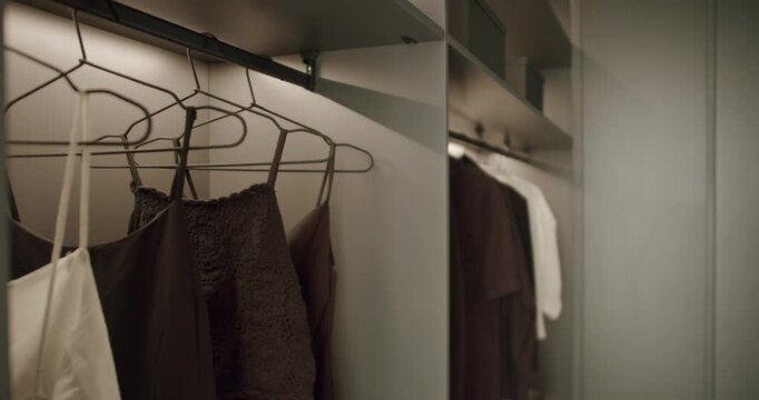 Clothes hanging in a modern, minimalist wardrobe. The neutral color palette and soft lighting create a calm and organized atmosphere. Perfect for showcasing fashion, storage solutions