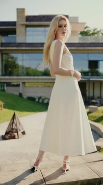 Elegant woman in white dress posing outdoors in front of a modern house on a sunny day. Captures sophistication, fashion, and contemporary lifestyle. Elegant Woman in White Dress