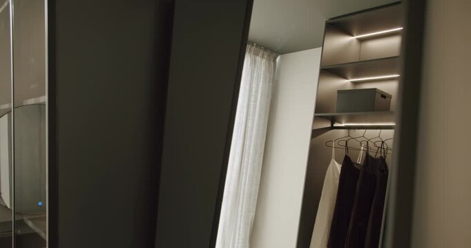 Modern walk-in closet with elegant dark wood and integrated lighting. Clothes neatly hang on a rail, with soft, sheer curtains adding a touch of luxury. This minimalist design