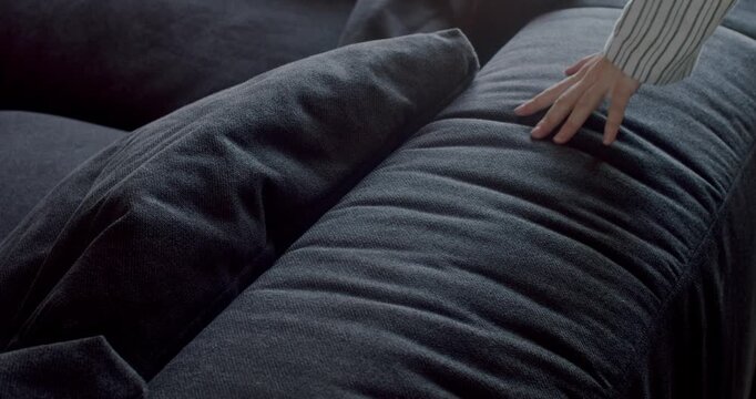 Woman's hand touches soft comfortable dark gray sofa. Close-up shot of female hand stroking new furniture in modern apartment. Cozy home, comfortable furniture, interior design showroom, new couch.