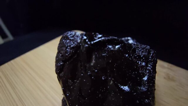 Cinematic macro shot of raw black Shilajit resin with a glossy, glass-like luster. This organic mineral exuding from Himalayan rocks features a dark, reflective texture and mysterious aesthetic.