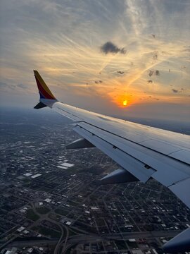 Aerial view from an airplane window during sunset with aircraft wing above a sprawling cityscape. Dramatic golden sky, clouds, and urban landscape create a scenic travel and transportation concept hig