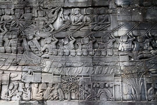 Detailed stone carvings illustrate crowded boats, warriors with spears, and daily life scenes at Bayon.  Siem Reap. Cambodia.