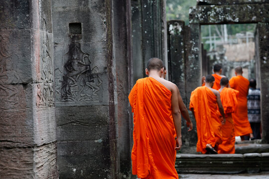 Group of monks in vivid robes stand and sit between mossy Bayon walls after visiting shrines.  Siem Reap. Cambodia.