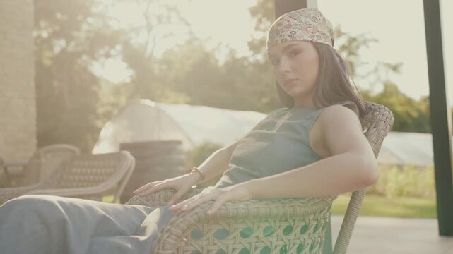 A woman relaxing outdoors in a rustic setting, wearing a headscarf and a relaxed dress. Sunlight creates a warm, peaceful atmosphere. Woman Relaxing Outdoors in a Rustic Setting with Sunlight