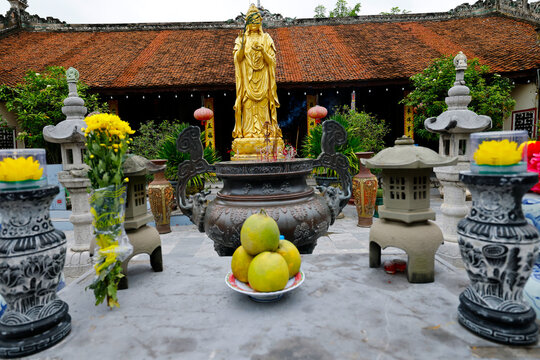 Phuc Lam Du Pagoda. Golden standing Guanyin statue in a temple courtyard with stone lanterns and fruit offerings. Haiphong. Vietnam.