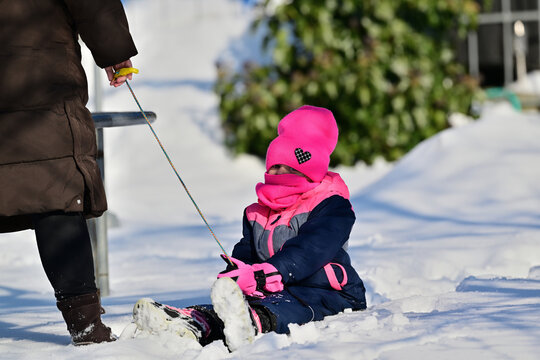 Little girl in a pink hat and scarf sledding in the snow