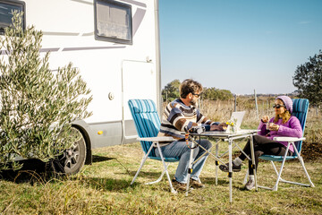 Fototapeta premium Couple working and relaxing outside their camper van while enjoying coffee on a countryside camping trip