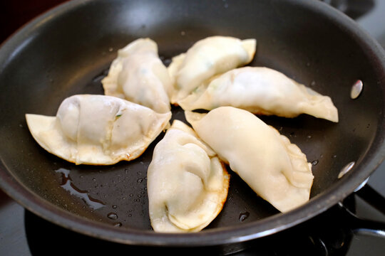 Dumplings cooking in a black non-stick frying pan, one flipped to reveal deep golden-brown crust.