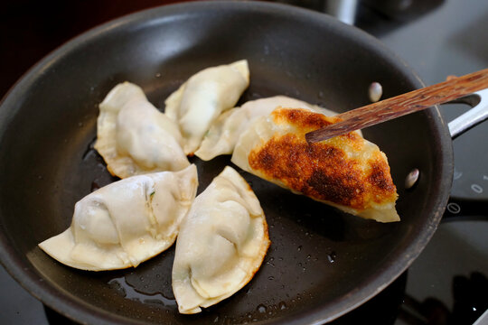 Dumplings cooking in a black non-stick frying pan, one flipped to reveal deep golden-brown crust.