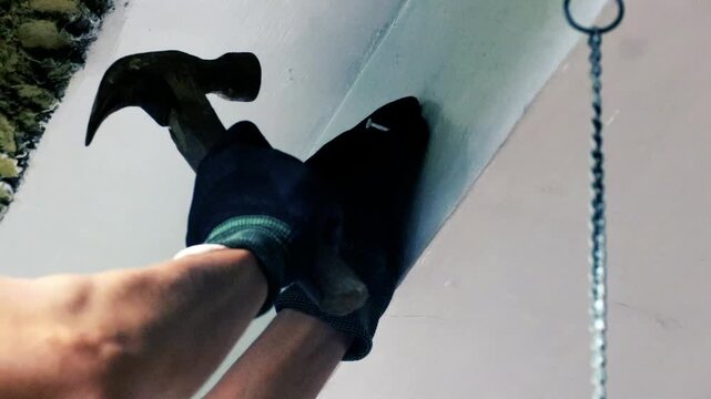 Gloved hand using hammer on wall surface, construction work, repair, DIY home improvement concept