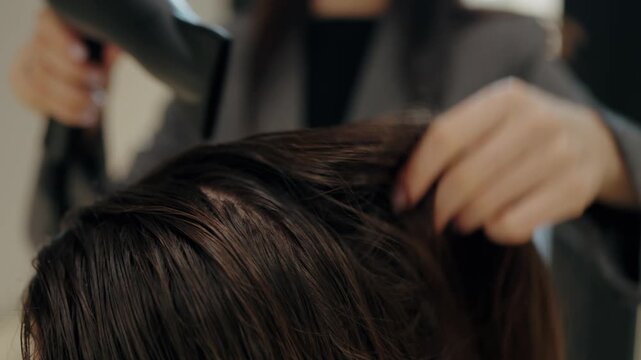 A professional stylist blow-dries a client's hair in a salon. The stylist works carefully, ensuring the hair is evenly dried and styled. The client appears relaxed and enjoys the pampering experience.