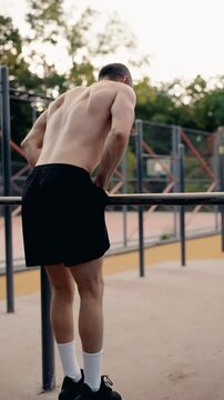 A muscular man performs dips on a horizontal bar at an outdoor gym. He demonstrates strength and fitness through this challenging calisthenics exercise.