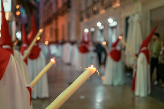Burning candles held by penitents (nazarenos) in red and white robes during a Holy Week (Semana Santa) night procession at Saint Nicholas Cathedral.
