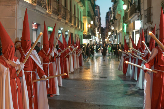 Burning candles held by penitents (nazarenos) in red and white robes during a Holy Week (Semana Santa) night procession at Saint Nicholas Cathedral.

