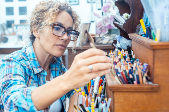 Woman artist selecting colored pencils in a home studio, concentrating on her creative drawing work