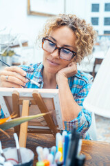 Middle-aged woman painting at an easel in a bright art studio, focused and relaxed creativity © simona