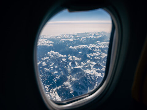 View from airplane window over the Alps mountain range covered with snow and clouds. Travel, aviation and scenic aerial landscape.