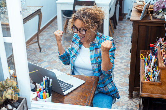 Happy woman celebrating success while working on a laptop in a colorful home office workspace