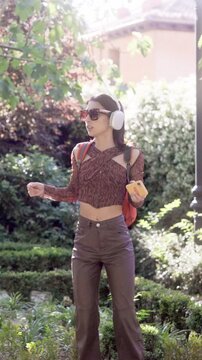 Joyful young woman dancing and listening to music in a sunny park