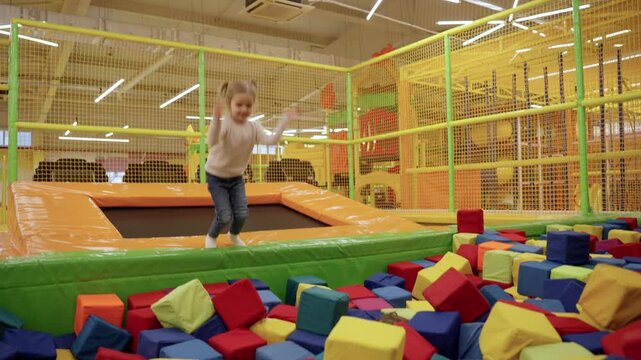 Two little girls playing on indoor playground in foam rubber pit in trampoline, active pastime in the amusement park. Slow motion