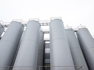 Low angle view of large industrial stainless steel silos and storage tanks at a food processing plant or brewery, modern manufacturing facility architecture © Rokas